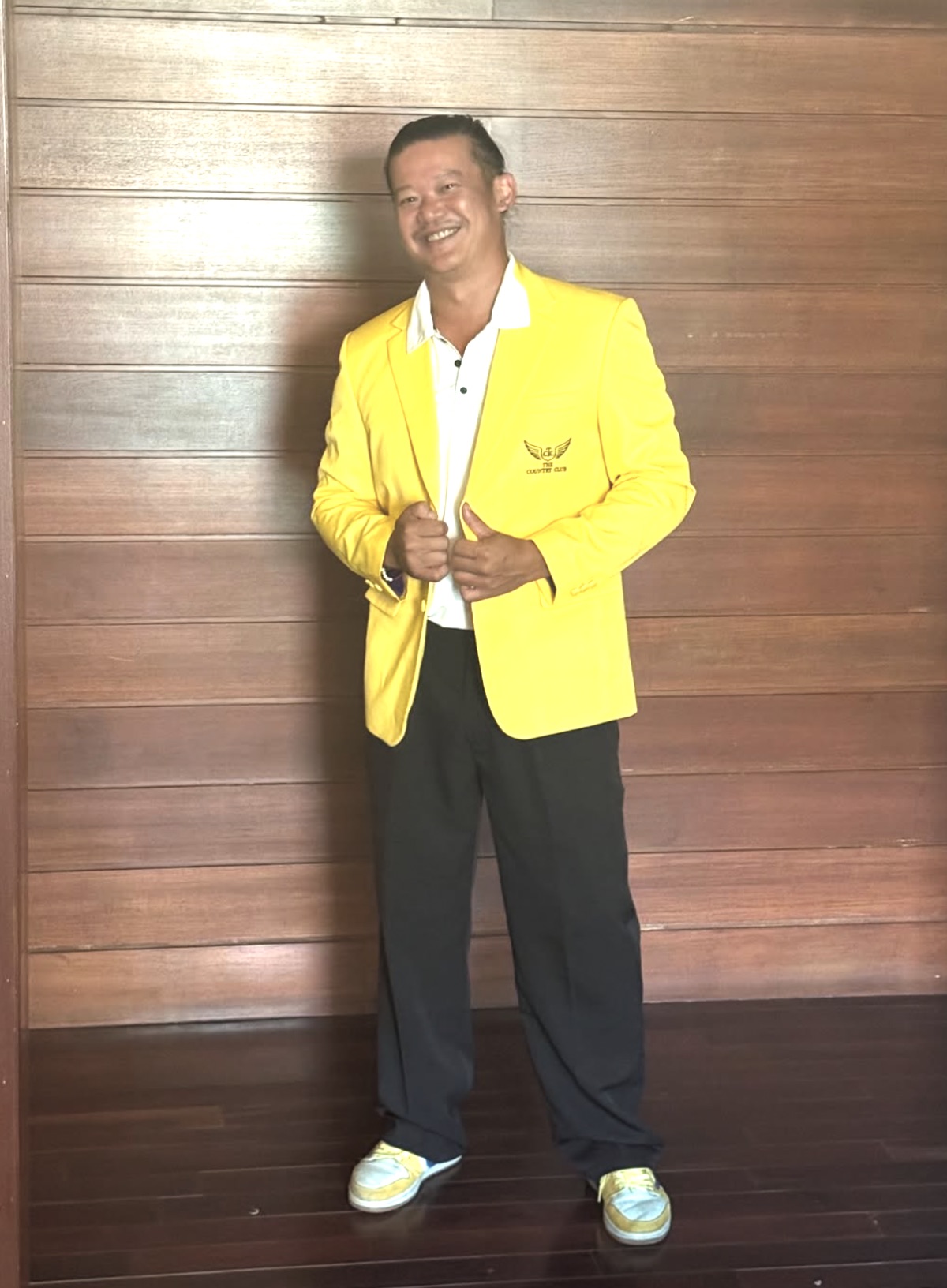 Boramy smiling in the one-of-one Country C1ub gold jacket with the gold wing crest, standing against a dark wood wall